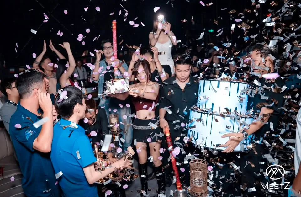 Bánh sinh nhật mang ra giữa sàn trong pháo giấy tại MeetZ